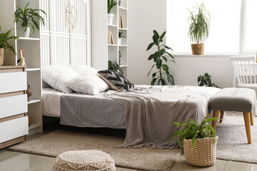 Cozy bed, shelving units and houseplants in interior of bedroom