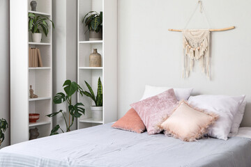 Cozy bed, shelving units and houseplants in interior of bedroom