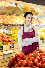 Female seller of fruit and vegetable store waits for visitors near counter and greets clients. Everyday life at shop working, customer support.