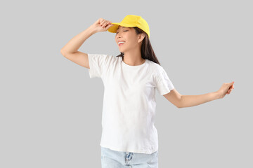 Young Asian woman in t-shirt and cap on grey background. Mockup for design