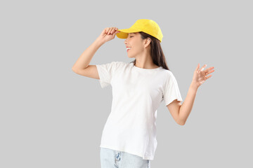 Young Asian woman in t-shirt and cap on grey background. Mockup for design