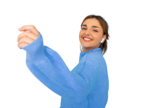 Smiling female in blue sweater dancing, enjoying music through wireless earphones, standing against transparent background