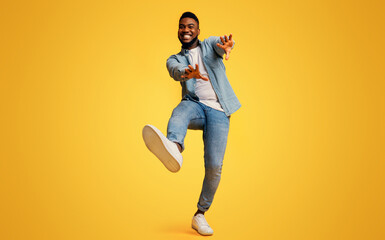 Funny african american guy dancing and extending his hands to camera over yellow studio background,...
