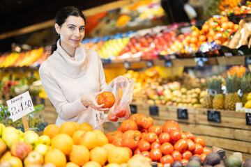 Customer puts the tomatoes in a plastic bag and prepares to weigh them before buying. Woman...