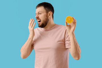 Sick young man with orange sneezing on blue background. Food Allergy Awareness Month