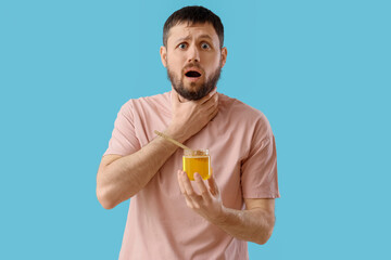 Shocked young man with honey on blue background. Food Allergy Awareness Month