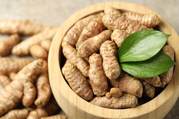 Tumeric rhizomes with leaves in bowl on grey table, closeup