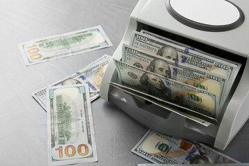 Money counter machine with dollar banknotes on grey textured table, closeup