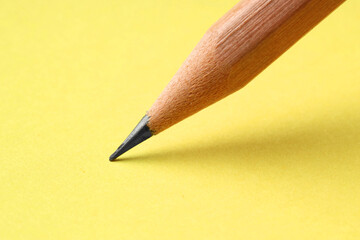 One sharp graphite pencil on yellow background, closeup