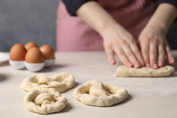 Woman making pretzel at white wooden table, closeup