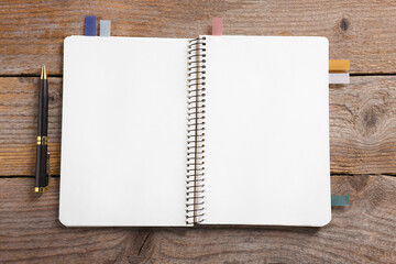 Open blank notebook with bookmarks and pen on wooden table, top view