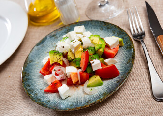 Delicious avocado salad with tomatoes, cheese and onions served on platter..
