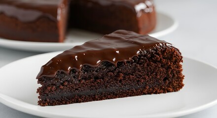 A slice of chocolate cake with glossy chocolate glaze on a white plate with cake in the background