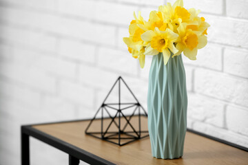 Vase with narcissus flowers and decor on dresser near white brick wall in living room, closeup