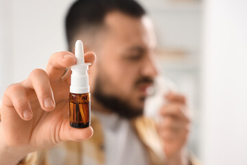 Sick young man with tissue and nasal drops suffering from allergy at home, closeup