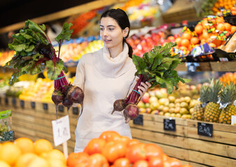 Young woman buyer choosing fresh beets in vegetable shop