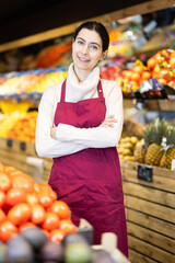 In sales hall of vegetable shop, visitors are greeted by seller woman. Staff at workplace willing to help, offering consultation and assistance.
