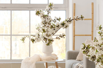 Vase with flowering branches on table in light living room
