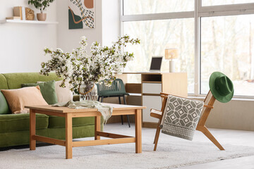 Interior of light living room with green sofa, armchair and flowering branches in vase