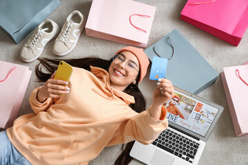Young woman with mobile phone and credit card shopping online on carpet, top view