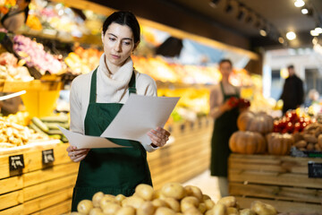 Female seller holds papers in her hands about the delivery of vegetables and fruits to the warehouse. Employee checks the quantity of products in the store