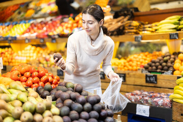 Customer puts the avocado in a plastic bag and prepares to weigh them before buying. Woman choosing ripe avocados in the vegetable section of a supermarket