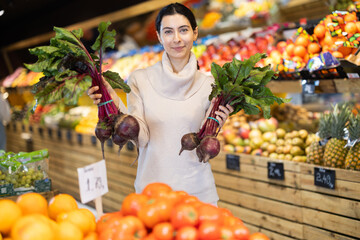 Woman holds raw beets in her hands near the counter in the vegetable section of the supermarket. Buyer chooses beetroot and vegetables