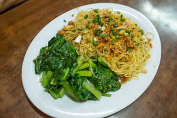 A simple dried egg noodle dish with fresh green vegetables served in a street food vendor in Thailand