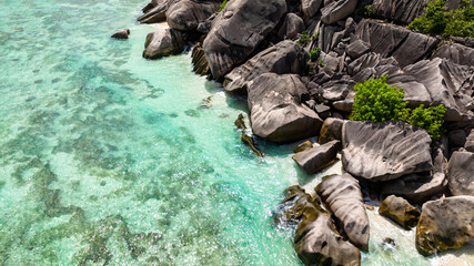 Granite rocks resting on white beach as the turquoise sea gently washes over. Seychelles, La Digue.
