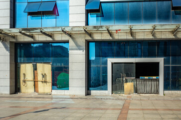 An abandoned commercial building in China with boarded-up glass doors, broken windows, and a...