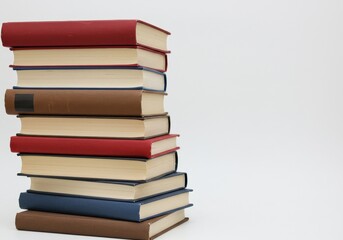 A stack of books with red blue and brown covers on a white surface in a vertical composition shot