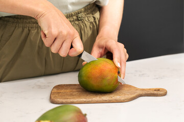 Person cutting ripe mango on wooden board for fresh summer snack preparation