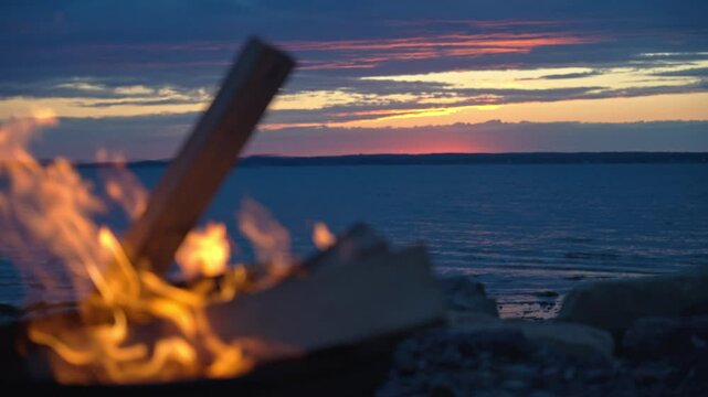 Flames of a firepit at dusk with ocean sunset on the horizon
