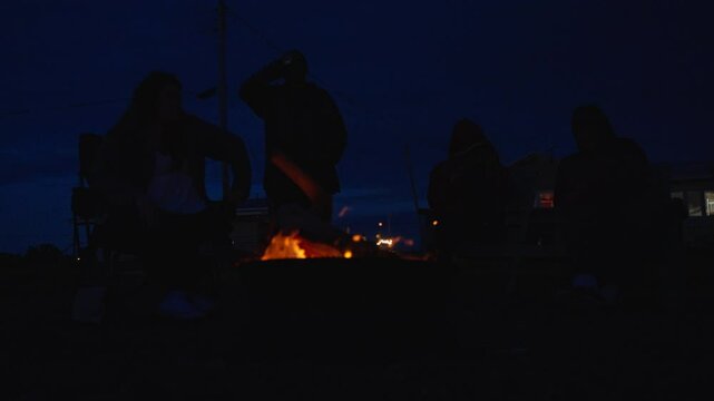 Friends gather around firepit at night enjoying drinks and relaxing outdoors