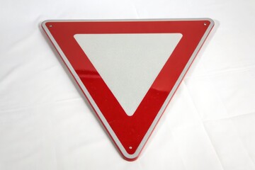 A triangular yield traffic sign with a red border and white center, placed on a white surface.
