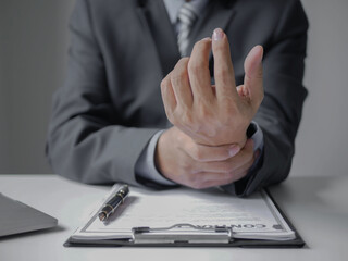 Obraz premium Asian businessman massaging his wrist due to pain from working on a computer keyboard for a long time. Wrist pain and numbness in the wrist area while working in the office