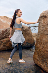 Athletic woman in gray workout apparel poses by the beach, showcasing confidence and health, emphasizing outdoor fitness and active lifestyle