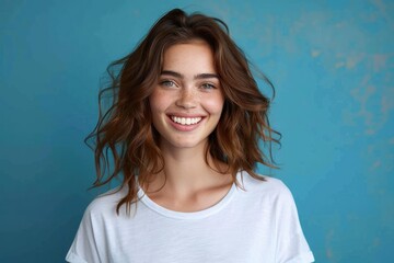 Fototapeta premium young woman with wavy brown hair wearing a white t-shirt standing against a blue textured background