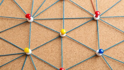 Colorful push pins and blue string form an interconnected network on a corkboard, symbolizing...