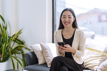 Smiling businesswoman using mobile phone while sitting on comfortable sofa in modern office space
