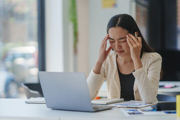 Asian office worker feeling tired and having a bad headache after working on computer for a long time