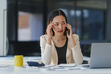 Young Asian manager touching her head, suffering from headache, having phone call conversation...