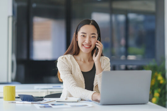 Young, happy professional multitasking with a laptop and mobile phone while working in a modern office environment