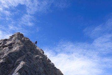 lone climber ascends steep rugged mountain face against clear blue sky
