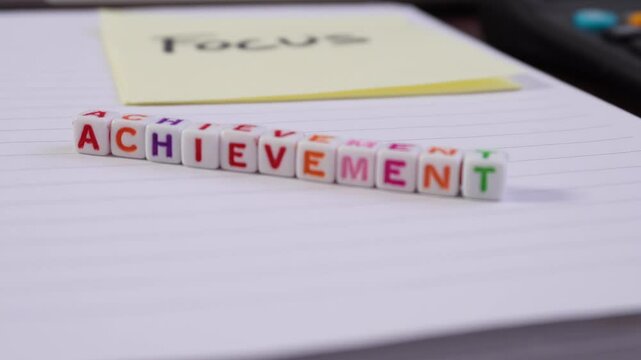 Blur and focus with the word "achievement" written on it. The cube is on a piece of paper, with the word Focus on a sticky note.