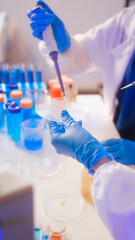 Two Asian female scientists wearing laboratory gloves sit at a table, carefully examining a test...