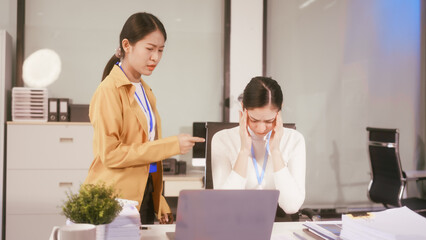 Two Asian women sit working at  desk,overwhelmed with stress struggling with headaches,feeling...