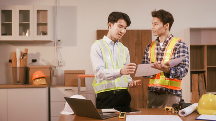 Two male engineers discuss a construction blueprint at a table in a modern office. They focus on architectural design, building structures, roofing,  wall details, planning for a contractor project