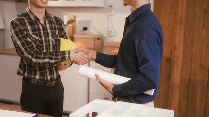 Two male engineers review blueprints in an office while discussing model house.They talk about construction projects, architectural design,roof structures,contractor coordination, building materials