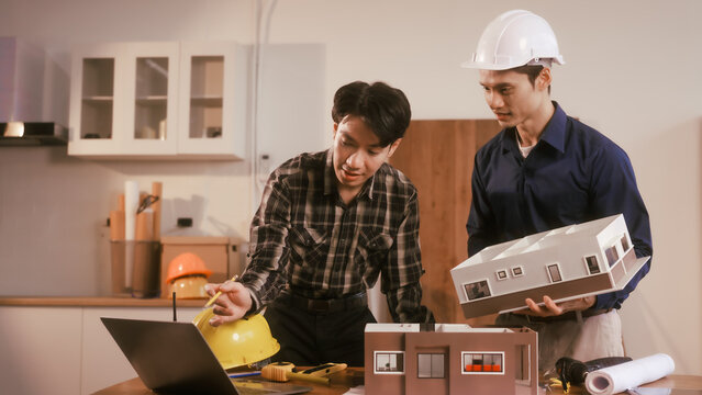 Two male engineers review blueprints in an office while discussing model house.They talk about construction projects, architectural design,roof structures,contractor coordination, building materials